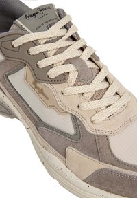 Beige og grå sneakers med mesh- og semsket skinnmaterialer, teksturerte detaljer, kremfargede lisser og logo på tungen. Skeidene har rund tå og mønstret såle.