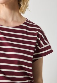 Maroon striped t-shirt made of cotton, featuring short sleeves and a round neckline with cream-colored stripes. Soft texture, casual design.