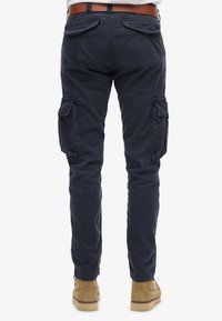 Pantalones cargo azul marino de algodón, con bolsillos laterales y traseros, diseño de pierna recta y dobladillo ajustado, combinados con zapatos marrones.