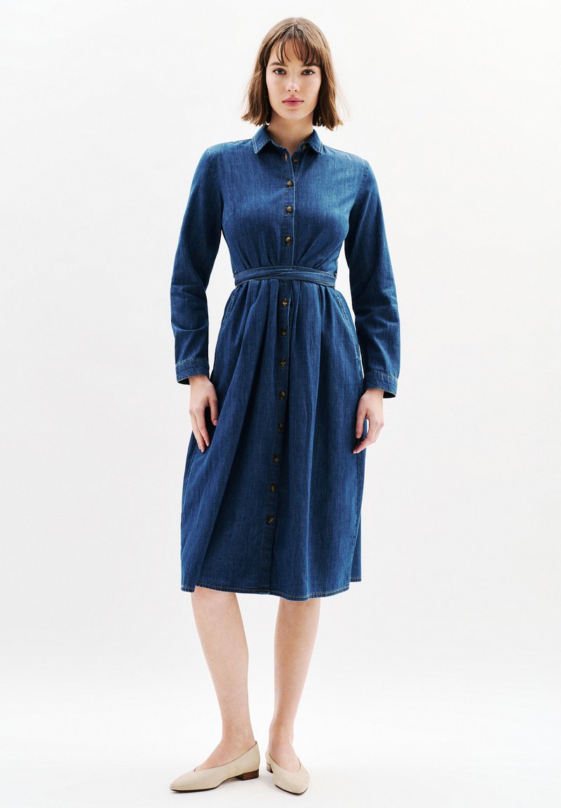 Dżinsowa sukienka koszulowa w ciemnoniebieskim kolorze, z długimi rękawami, z przodu zapinana na guziki, z wcięciem w talii i spódnicą do kolan. Posiada klasyczny kołnierzyk i subtelną teksturę.