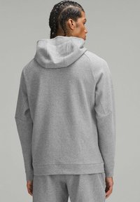 Szara bluza z kapturem z teksturowanej tkaniny, z kieszenią typu kangur i kapturem. Ma luźny krój oraz ścięgna przy mankietach. W połączeniu z dopasowanymi szarymi spodniami.