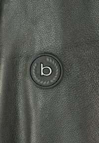 Čierna kožená textura s kruhovým logom, ktoré obsahuje malé písmeno 'b' a vavrínové akcenty. Povrch vyzerá mierne lesklý a hladký.