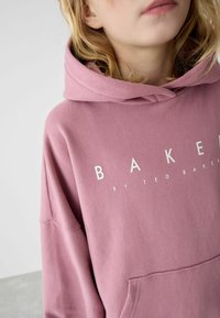 Felpa con cappuccio rosa e tasca frontale. Presenta una scritta bianca in grassetto "BAKER" sul petto. Tessuto morbido e textured con vestibilità comoda.