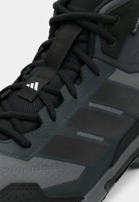 Αθλητικό παπούτσι σε μαύρο και γκρι με υφαντό επάνω μέρος, συνθετικές επικαλύψεις και τρεις έντονες ρίγες στη πλευρική πλευρά. Διαθέτει επίπεδα κορδόνια.