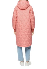 Gepolsterter rosa Mantel mit einem Rautenmuster, ausgestattet mit einer Kapuze und gerippten Bündchen. Kombiniert mit hellblauen Jeans und weißen Sneakers.