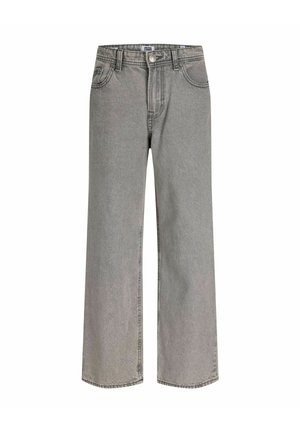 Teenager iført en mørk denimjakke, lysegrå jeans, sorte sko, beige t-shirt og en grå kasket, står og smiler mod en ensfarvet baggrund.