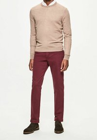 Pull en tricot marron clair, pantalons bordeaux et bottes en daim marron foncé. Design simple et coupe ajustée avec une texture lisse.