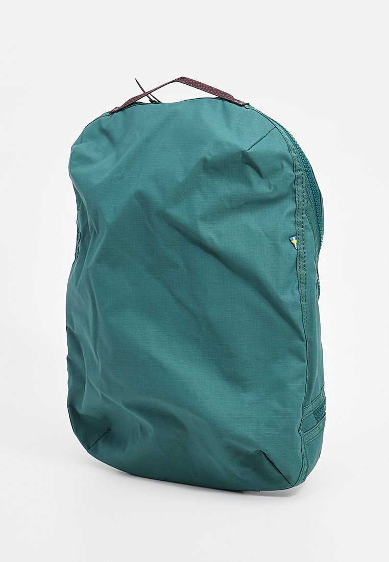 Teal-farbene weiche Stofftasche mit einem schwarzen und roten Griff oben, sichtbarem seitlichen Reißverschluss und kleinem schwedischen Flaggenanhänger auf der rechten Seite.