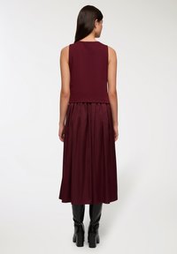 Burgundowa sukienka składająca się z dwóch części, z dopasowaną górą oraz plisowaną spódnicą do ziemi. Wykonana z gładkiego materiału, zestawiona z czarnymi botkami na wysokim obcasie sięgającymi do kolan.