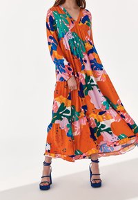 Färgg landlords lång klänning med V-ringning, långa ärmar, lagerdesign och abstrakta blommönster i orange, rosa, grönt och blått.