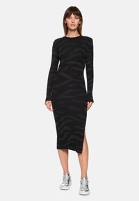 Black knit dress with long sleeves, featuring a subtle zebra pattern and a side slit. Paired with silver athletic sneakers.