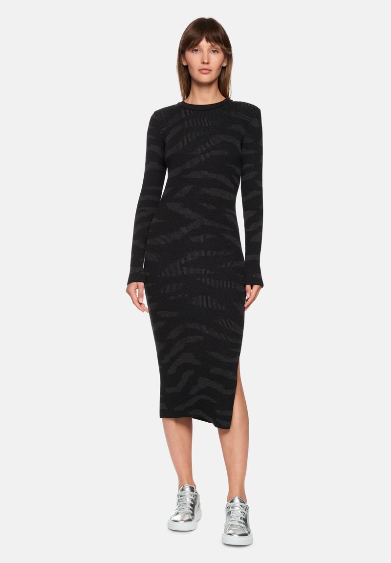 Black knit dress with long sleeves, featuring a subtle zebra pattern and a side slit. Paired with silver athletic sneakers.