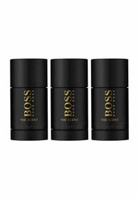 Kolme sylinterimäistä mustaa deodoranttipulloa, joissa on kultainen teksti "BOSS HUGO BOSS THE SCENT", jokainen merkitty 75 ml ja 70 g.