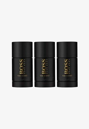 Tre cylindrisk sorte deodorantstænger med guldtekst, der står "BOSS HUGO BOSS THE SCENT," hver mærket med 75 ml og 70 g.