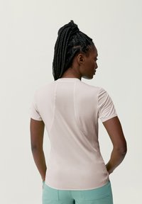 Krátky rukáv, svetloružový športový top s textúrovanou látkou a nenápadným švom, skombinovaný so svetlozelenými nohavicami.