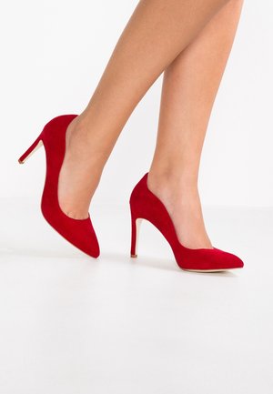 Røde ruskindshælede sko med spids tå og slank stiletthæl, der har en glat tekstur og et minimalistisk design.