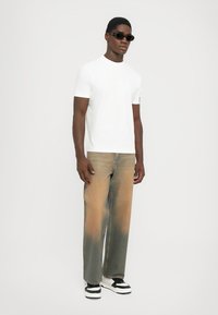 Vit bomulls-t-shirt i kombination med lösa, blekta ljusbruna jeans. Svarta solglasögon och svart-vit sneakers fulländar looken.