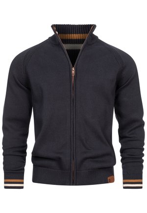 Donkerblauwe ritstrui met een geribde kraag. Heeft contrasterende crèmekleurige en bruine strepen op de kraag en manchetten. Textuur gebreide stof.