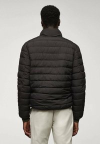 Giacca a vento nera con un design trapuntato, dotata di un colletto alto e polsini a coste. Il materiale sembra liscio e leggero.