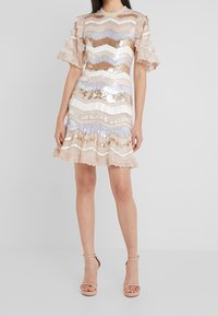 Robe à manches courtes, longueur genoux, avec un motif en zigzag en sequins et un bord en dentelle. Les couleurs incluent beige, rose et bleu clair.