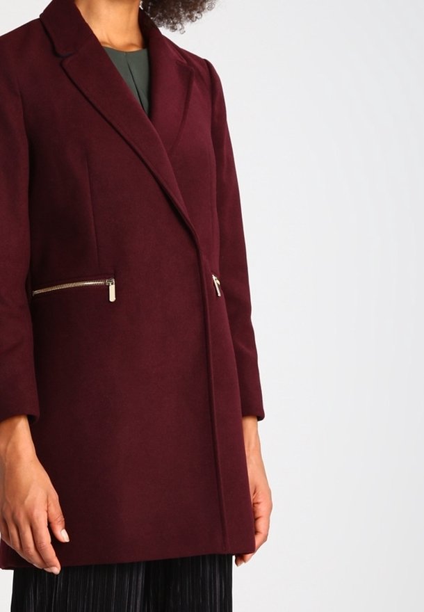 Burgundyröd ullblandad kappa med en figursydd design, notched krage och två dragkedjefickor. Slät yta, medellång, med skräddarsydda ärmar.