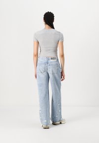 Camiseta ajustada de color gris claro combinada con jeans sueltos de color azul claro desgastados, con pierna ancha, dobladillo deshilachado y una etiqueta de marca en la cinturilla.