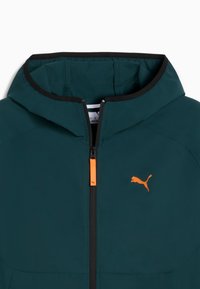 Chaqueta con capucha de color verde azulado, fabricada en un tejido suave, que presenta un cierre frontal con una cremallera naranja y un ribete negro; logo de Puma en naranja.