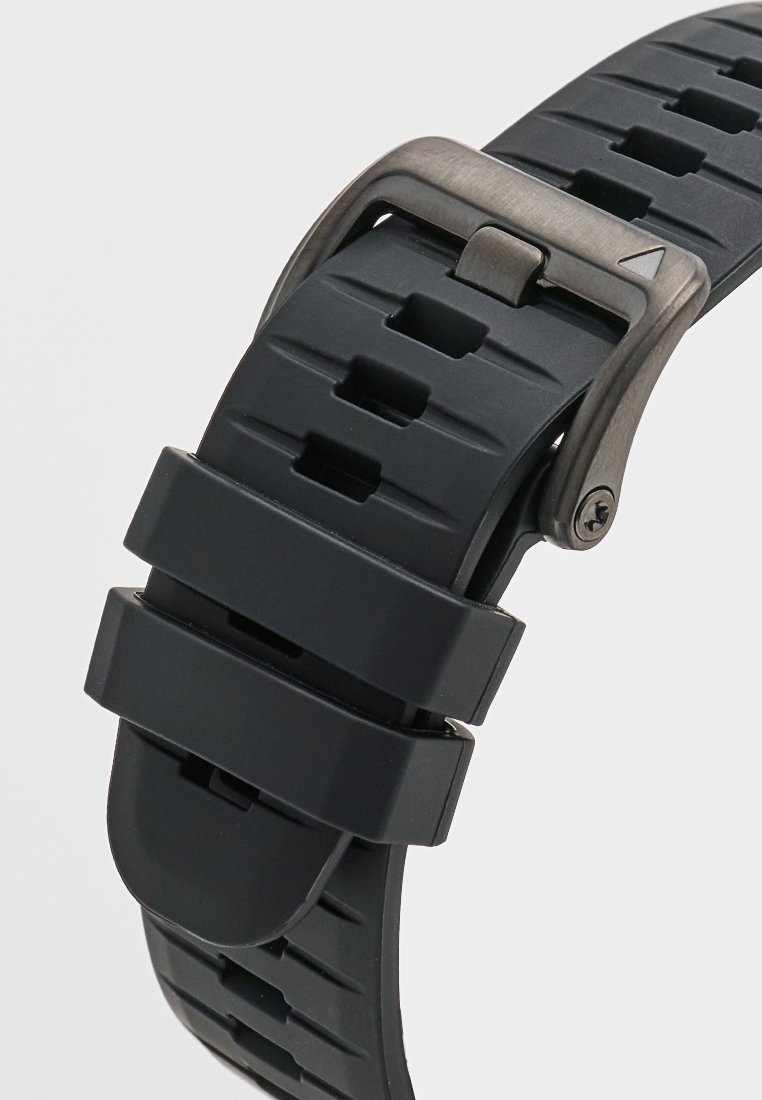 Correa de reloj de goma negra con un diseño texturizado, orificios rectangulares y una hebilla de metal con un detalle en forma de flecha.