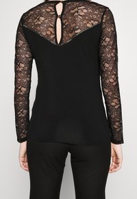 Zwart top met lange kantmouwen, voorzien van een kantensluiting aan de achterkant, een sleutelgatuitsnijding en een soepel stoffen lijfje. Eenvoudig en elegant ontwerp.