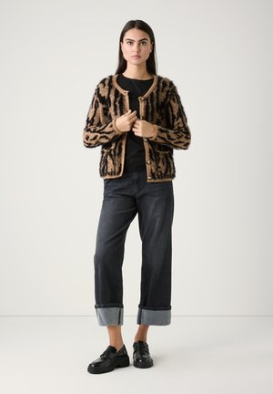 Fuzzy bruine en zwarte geblokte cardigan met een ronde hals, knoopsluiting, gedragen over een zwarte top, gecombineerd met donkere spijkerbroeken en zwarte instappers.