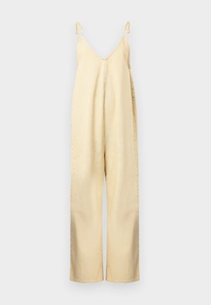 Μπεζ ολόσωμη φόρμα με φαρδιά παντελόνα, ρυθμιζόμενες λεπτές τιράντες και βαθύ V λαιμόκοψη, κρεμασμένη σε απλό λευκό φόντο.