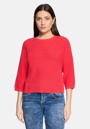 Roter, strukturierter Pullover mit Dreiviertelärmeln, Rundhalsausschnitt und geradem Saum, kombiniert mit blauen Jeans.