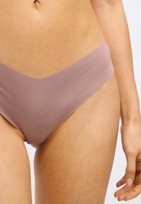 Licht mauve bikinionderdeel gemaakt van gladde stof, met een v-vormige taille en naadloze randen voor minimale zichtbaarheid onder kleding.
