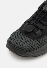 Sneaker nera con tomaia in rete, dotata di punta testurizzata, lacci elastici e chiusura con toggle rotondo. Suola in gomma rinforzata per una maggiore durata.
