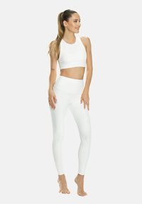 Conjunto de ropa deportiva blanca que incluye un top corto con un cuello alto y leggings de talle alto. Textura suave, diseño ajustado y costuras mínimas.