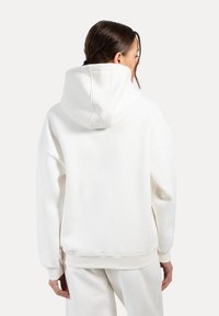 Felpa bianca oversize con un ampio cappuccio, polsini e orlo a costine. Realizzata in un tessuto morbido, presenta una texture liscia e un design minimalista.