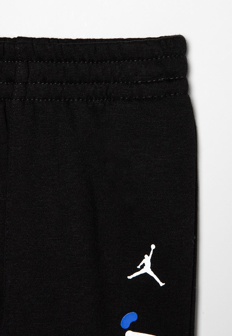 Pantalones de chándal negros con una cintura elástica, tejido suave y un logo blanco de Air Jordan con acentos en azul y negro cerca del dobladillo.