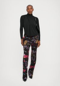 Zwarte lange mouwen top met asymmetrisch ontwerp; bloemenpatroon broek in zwart, roze en blauw; stiletto hakken en kleine zwarte tas.