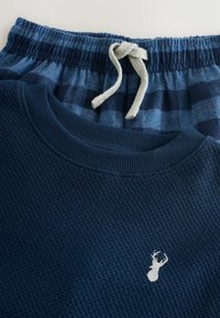 Navy blue waffle-knit sweatshirt with a small deer logo, paired with blue checkered pajama pants featuring an elastic waistband and drawstring.