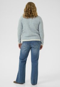 Light blue patterned sweater with long sleeves, paired with flared blue jeans. The back view displays a textured knit and a relaxed fit.