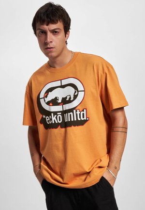 Oranžové bavlnené tričko s veľkým čiernobielym grafickým motívom nosorožca a textom "*eckō unlt.d." pod ním v tučnom písmene. Krátke rukávy a voľný strih.