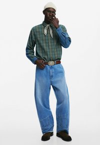 Zielono-niebieska koszula w kratę z długim rękawem, jasnoszary szalik, oversize'owe jasnoniebieskie dżinsy, brązowy pasek z srebrną klamrą i czarne buty.