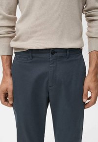 Tmavě šedé kalhoty mají klasický střih, hladkou látku, přední kapsy a kovové zapínání na knoflík v pase.