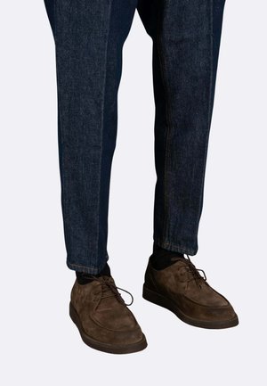 Scarpe stringate in suede marrone con punta rotonda, abbinate a jeans denim blu scuro a gamba dritta, con cuciture a contrasto alle cuciture.