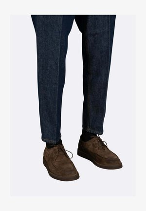 Scarpe stringate in suede marrone con punta rotonda, abbinate a jeans denim blu scuro a gamba dritta, con cuciture a contrasto alle cuciture.