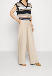 Virkat randigt tröja i marinblått, beige och vitt med V-hals; kombinerat med högmidjade beige vida byxor; öppetåiga bruna sandaler.