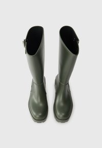 Groene rubberen regenlaarzen met een gladde afwerking, rechte schacht en een gestructureerde zool. Zijdetails met gespsluiting nabij de bovenkant van de laars.