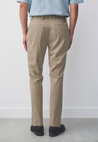 Pantalon beige sur mesure avec une texture côtelée subtile, doté de poches arrière et d'une coupe standard, associé à des chaussures noires.