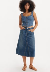 Jeanscropped topp med firkantet halslinje og knaplukning, parret med et højtaljet jeansskørt med en frontslids. Brune strop sandaler.