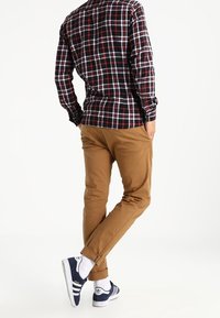 Rutig långärmad skjorta i svart, röd och vit, ihop med tanfärgade chinos och blå Adidas sneakers. Vita strumpor synliga.